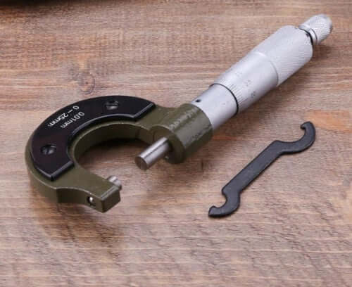 0 to 25mm, Metric micrometer on a wooden surface showing its applicable adjustment key.